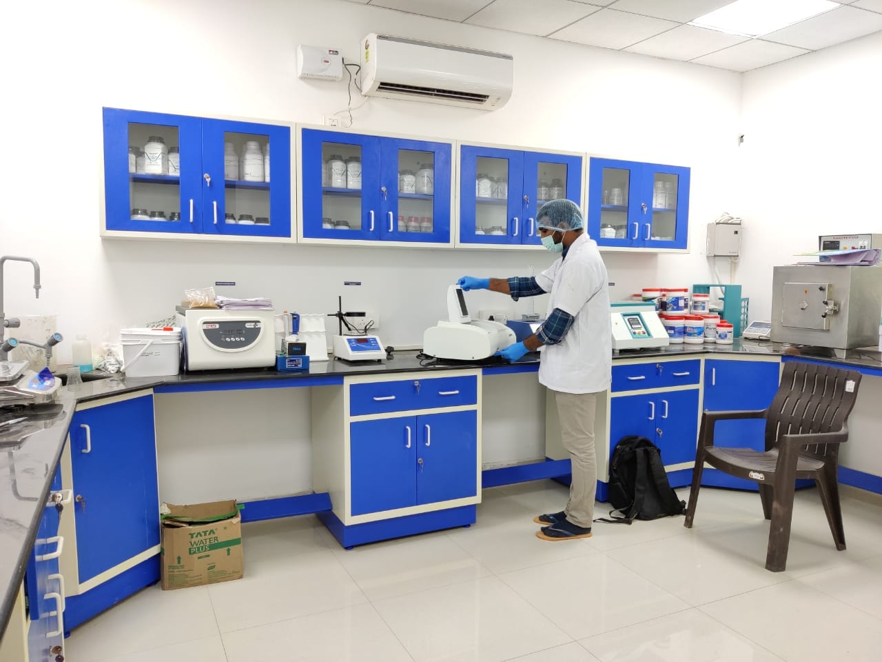 R&D laboratory with blue cabinets and a technician analysing samples at the instruments bench